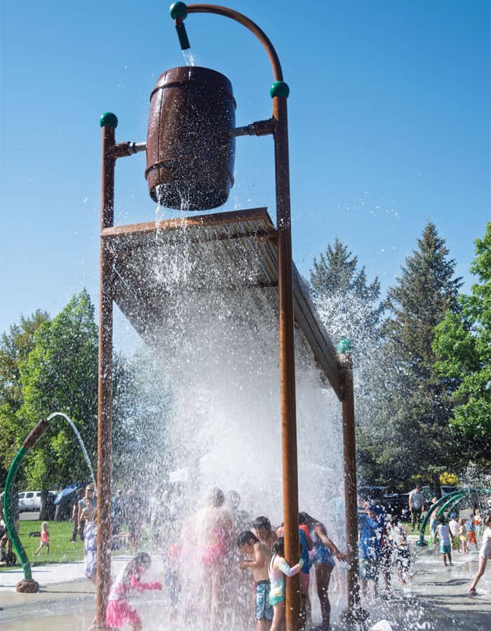 large, brown dumping bucket splashing water on children on a splash pad