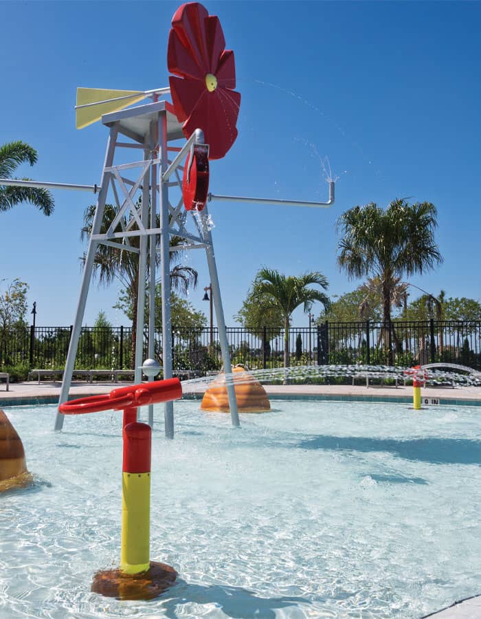 a shallow swimming pool with red and yellow water cannons, rock-themed sprayers, and a red windmill-themed water feature