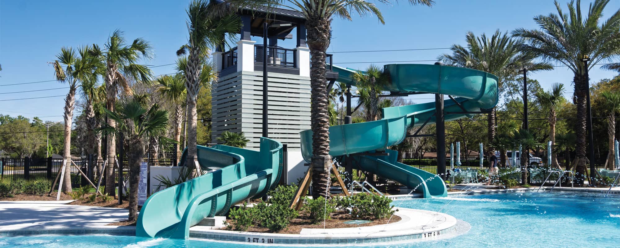 a small blue waterslide and a large blue waterslide that empty into a swimming pool in a tropical landscape