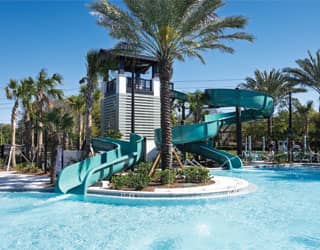 a small blue waterslide and a large blue waterslide that empty into a swimming pool in a tropical landscape