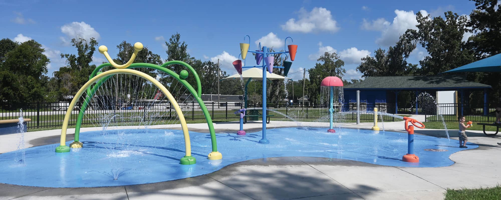 colorful splash pad design featuring interactive water toys including spray rings, water cannons, dumping buckets, a mushroom water feature. and ground sprays