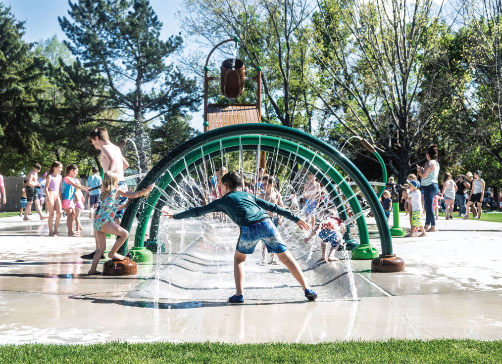 a child interacting with spraying jets on a splash pad with spray rings and a large dumping bucket