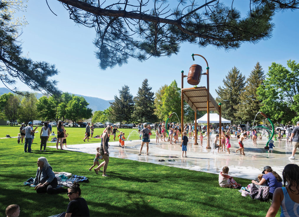 a large crow of people gather at a splash pad in a park