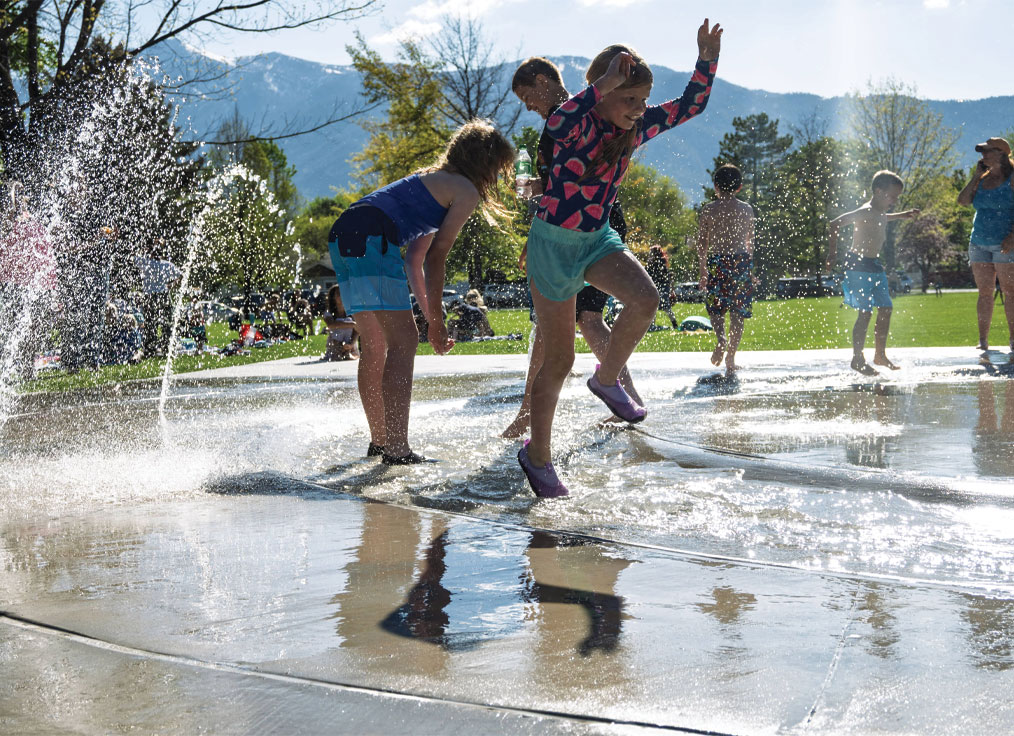 a child leaps into a river water feature on a splash pad surrounded by arching jets of water