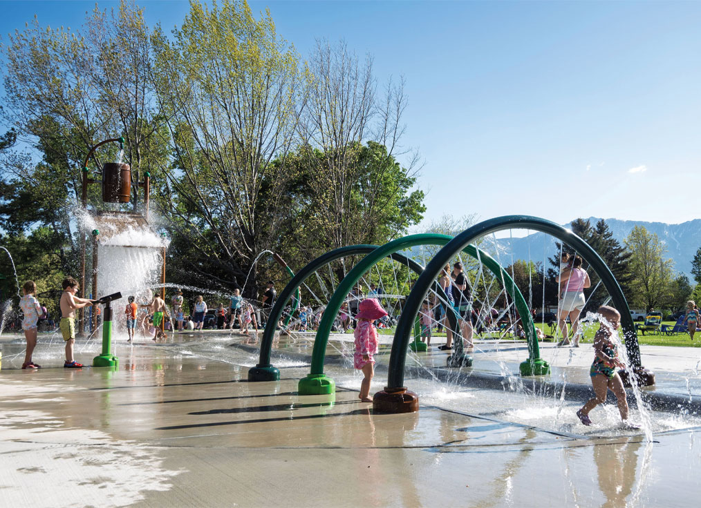 children playing on a splash pad with spraying rings, shooting water cannons, and a large dumping bucket
