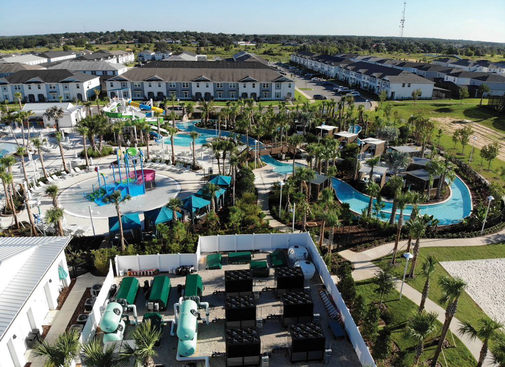 overhead view of a waterpark with a large swimming pool hydraulic equipment yard, multi-level water playset, lazy river, and double flume waterslide
