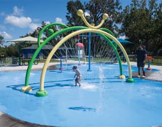 child running through yellow and green spray rings on a splash pad