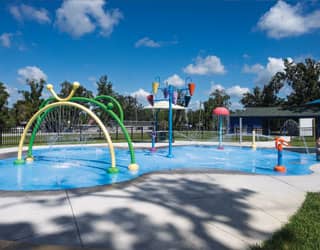 colorful splash pad design featuring interactive water toys including spray rings, water cannons, dumping buckets, a mushroom water feature. and ground sprays