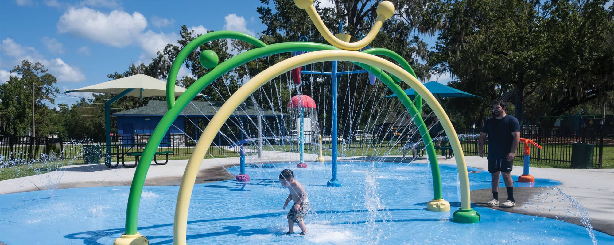child running through yellow and green spray rings on a splash pad