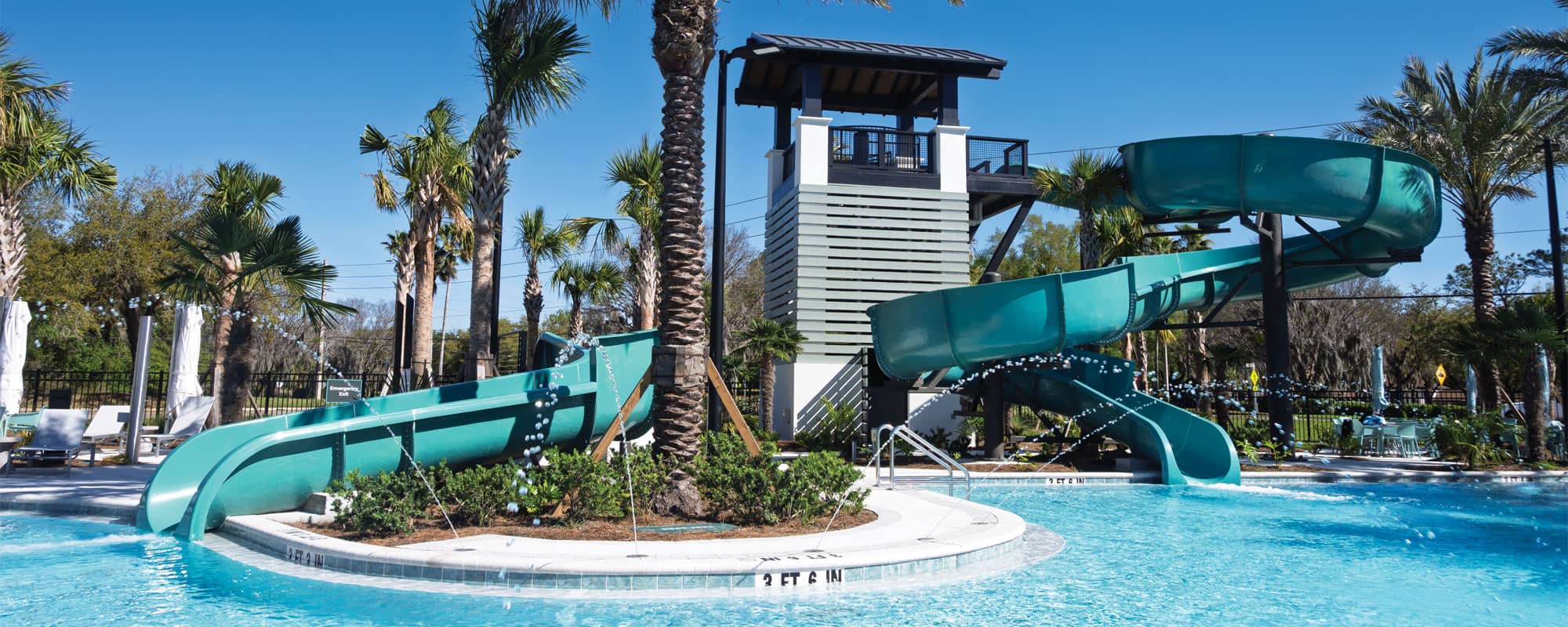 swimming pool with a small and large blue waterslide in a tropical setting