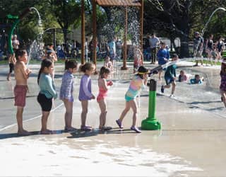 children lined up to play with a water cannon on a splash pad