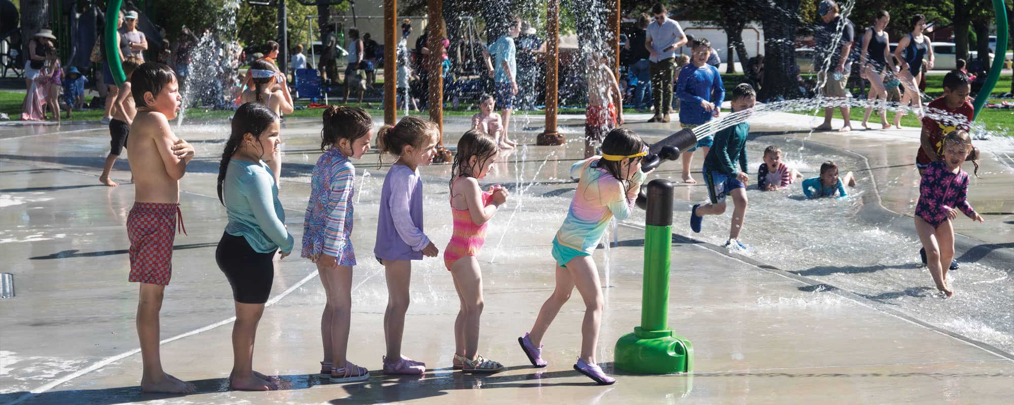 children lined up to play with a water cannon on a splash pad