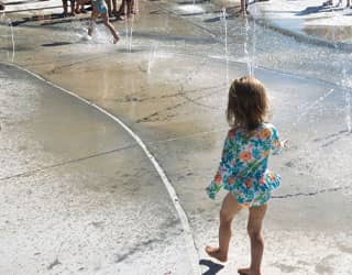 a young child exploring the ground sprays on the splash pad