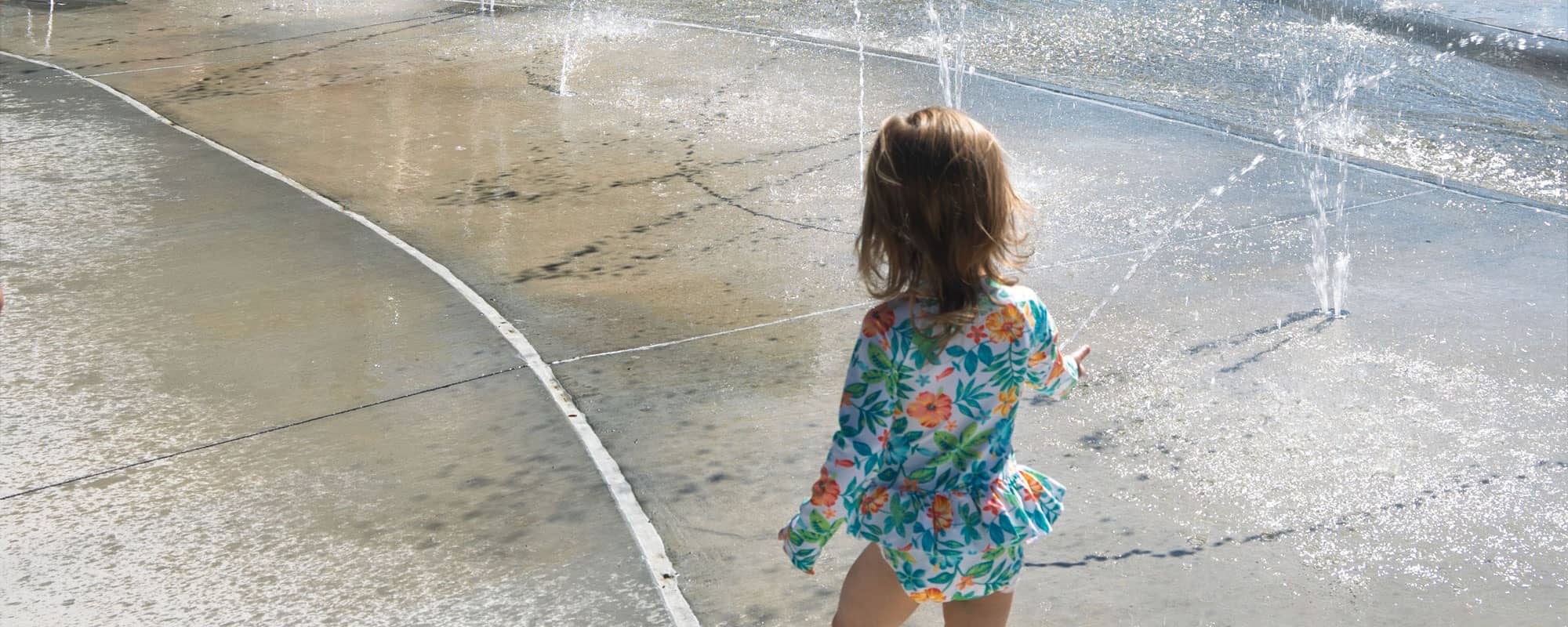 a young child exploring the ground sprays on the splash pad