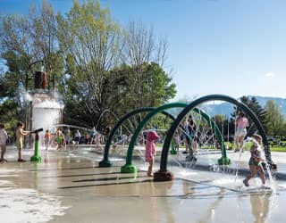 children interacting with a water cannon, spraying rings, and a large dumping bucket on a splash pad