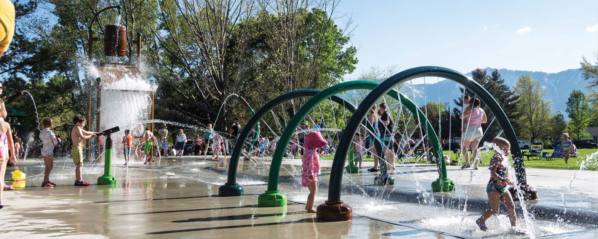 children interacting with a water cannon, spraying rings, and a large dumping bucket on a splash pad