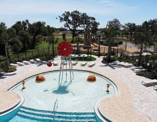 overhead view of a water play area in a swimming pool with a red windmill-themed spray feature and a dry playground in the background