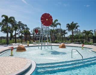 windmill-themed spray feature, rock-themed spray features, and water cannons in a shallow swimming pool
