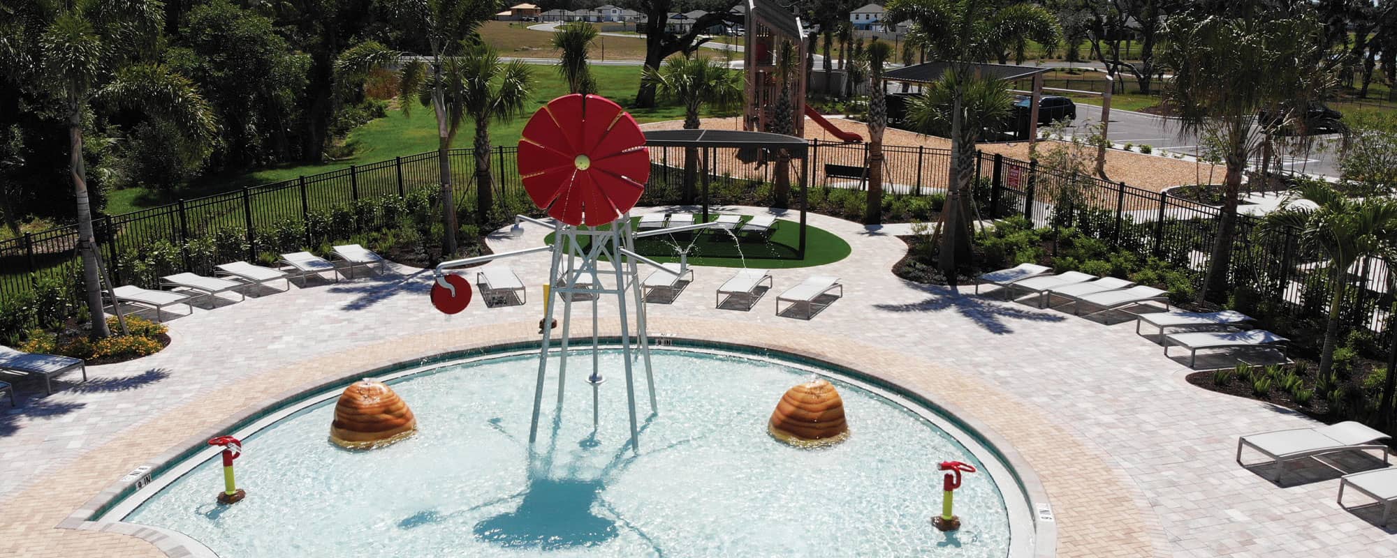 overhead view of a water play area in a swimming pool with a red windmill-themed spray feature and a dry playground in the background