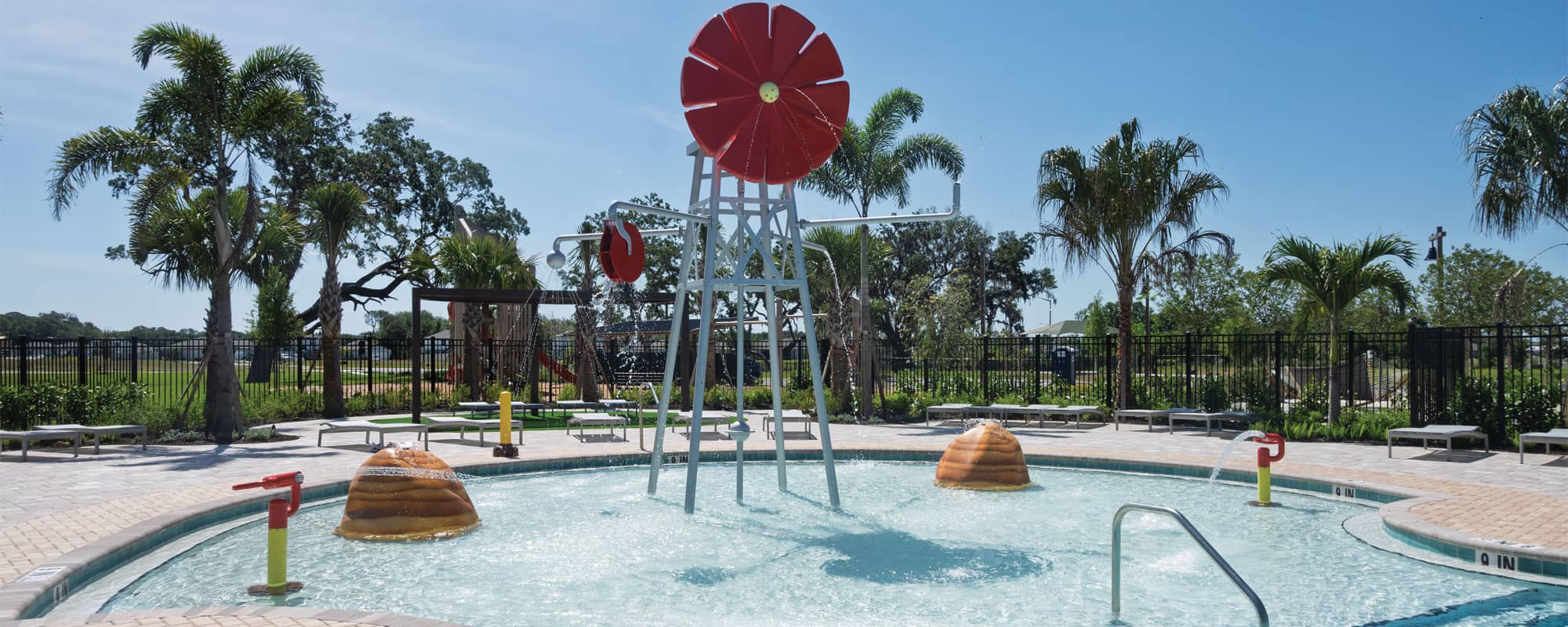 windmill-themed spray feature, rock-themed spray features, and water cannons in a shallow swimming pool