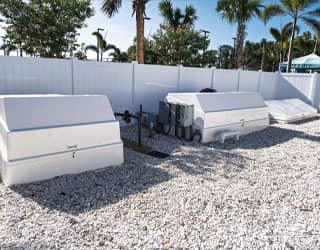 white swimming pool filtration equipment packs are housed in a gated, outdoor equipment yard