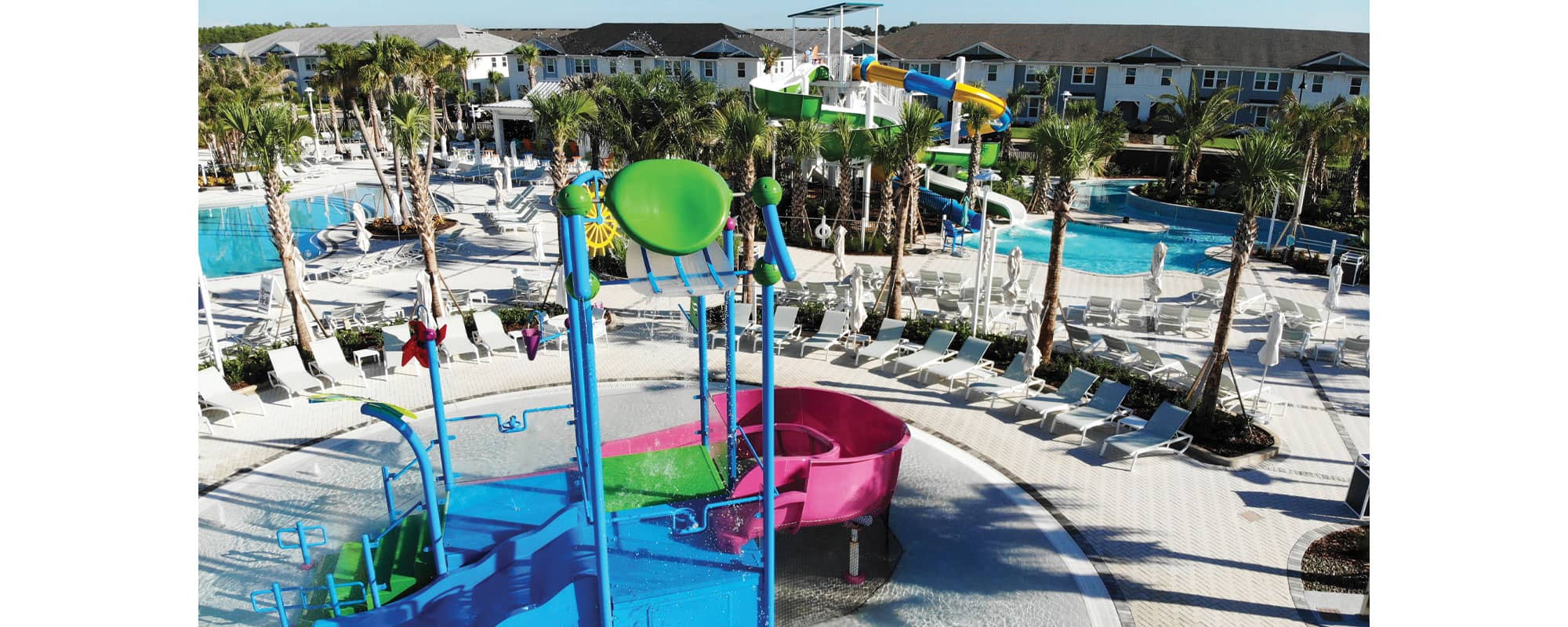 interactive multi-level water play structure with a waterslide in the background in a tropical setting