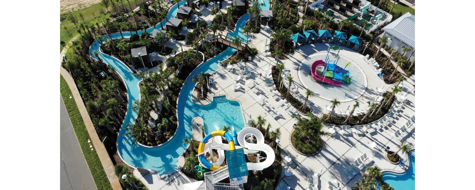 overhead view of community waterpark with waterslides, lazy river, kiddy pool with a multi-level water play structure, and a state-of-the-art filtration equipment yard