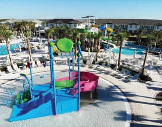 interactive multi-level water play structure with a waterslide in the background in a tropical setting