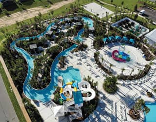 overhead view of community waterpark with waterslides, lazy river, kiddy pool with a multi-level water play structure, and a state-of-the-art filtration equipment yard